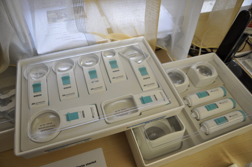 Ein Set von Lupen und Sehhilfen in einer Schachtel, die auf einem Tisch liegt, zur Unterstützung von Menschen mit Sehbehinderungen.