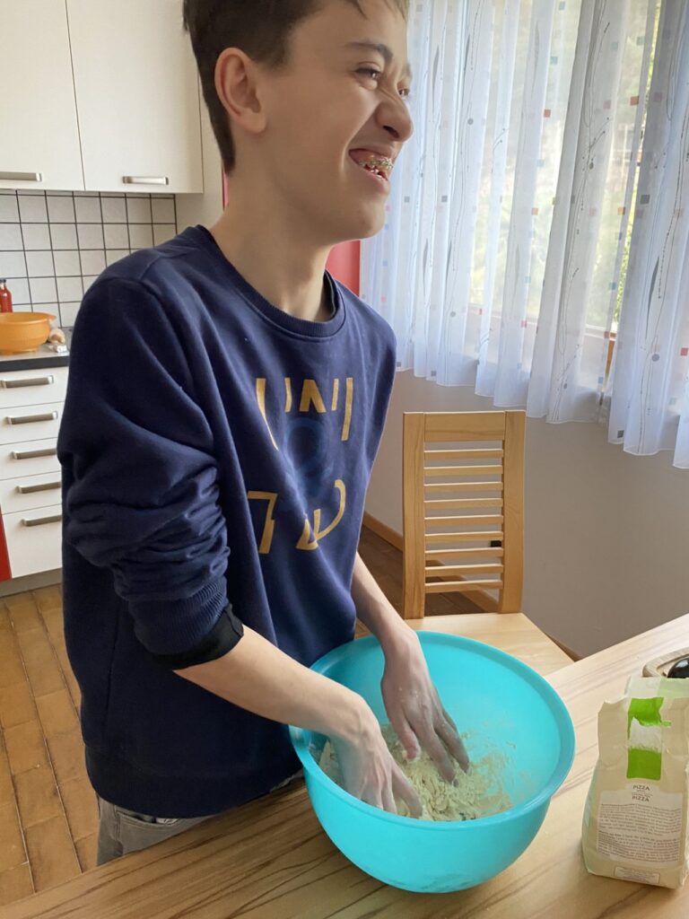 Ein lächelnder Junge knetet Teig in einer blauen Schüssel in einer Küche.