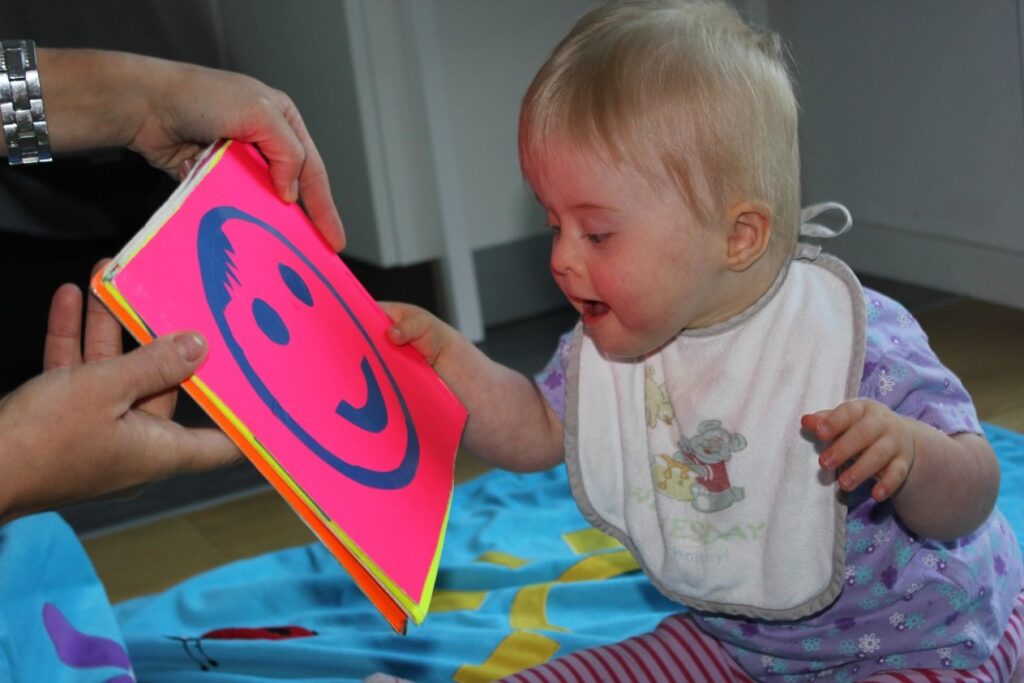 Ein kleines Kind betrachtet neugierig ein Buch mit einem großen, gezeichneten Smiley-Gesicht.