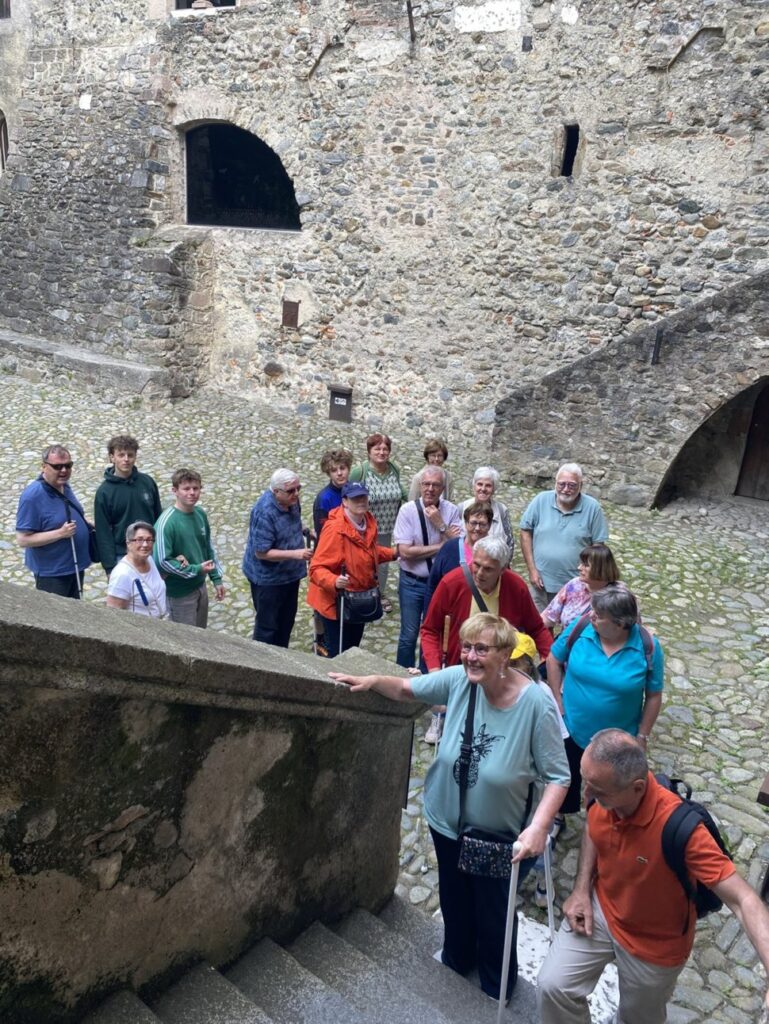 Eine Gruppe von Menschen steht auf einem gepflasterten Platz vor einer alten Steinmauer, einige davon mit Blindenstöcken.