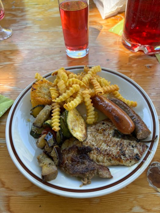 Teller mit gegrilltem Fleisch, Gemüse und Pommes frites auf einem Holztisch