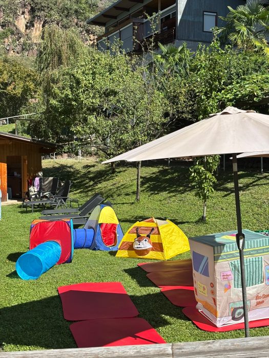 Spielbereich mit bunten Zelten, einem Tunnel und Matten auf dem Rasen