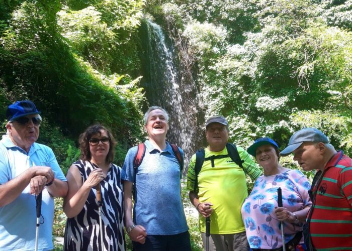 Eine Gruppe von Menschen steht lächelnd vor einem Wasserfall im grünen Wald.