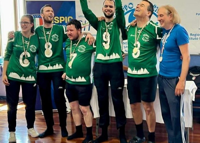 Sechs Personen in grünen Sporttrikots und Medaillen feiern gemeinsam und halten einen großen Pokal in die Luft.