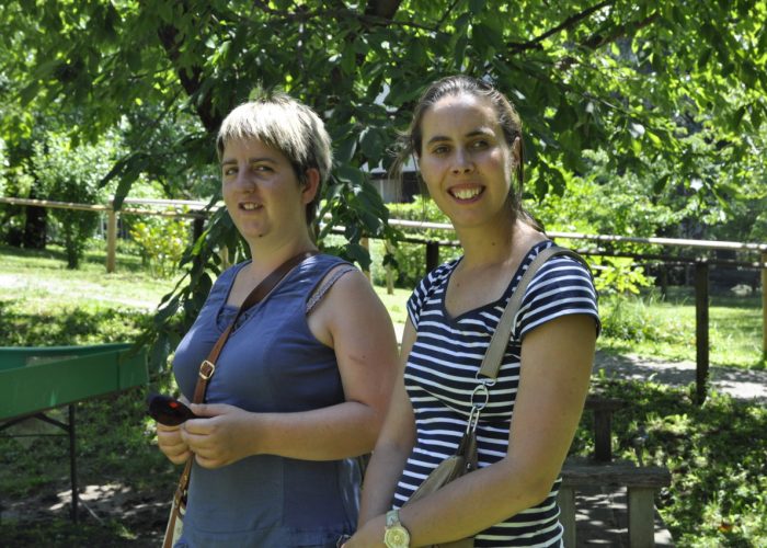 Zwei lächelnde Personen stehen an einem sonnigen Tag in einem grünen Park.