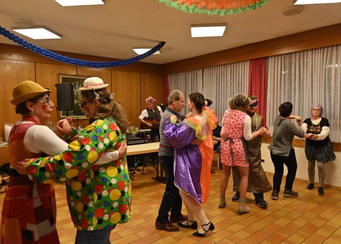 Menschen in bunten Kostümen tanzen fröhlich in einem dekorierten Raum.